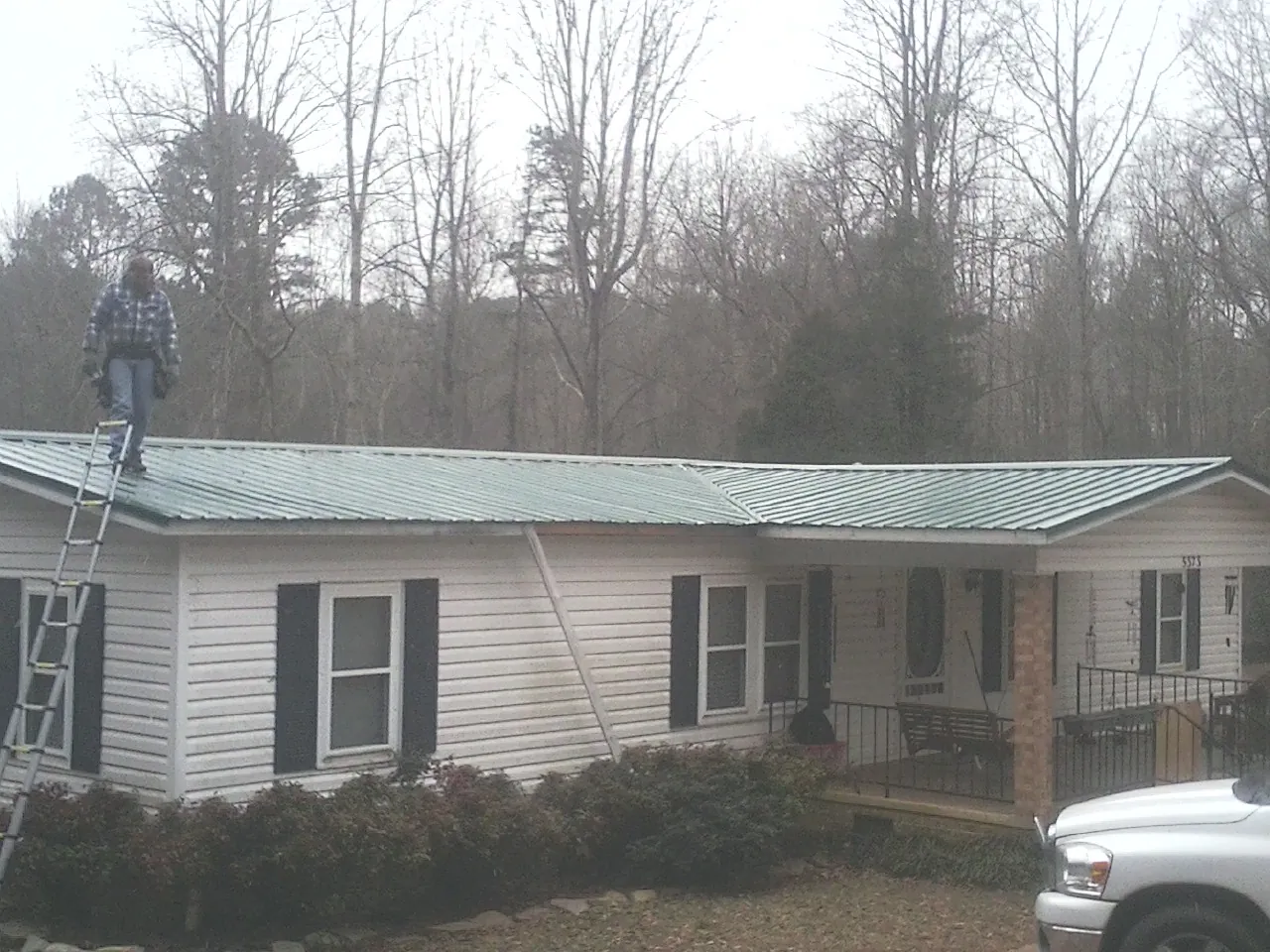 Worker on a ladder beside a new green metal roof on a ranch home in Rockford