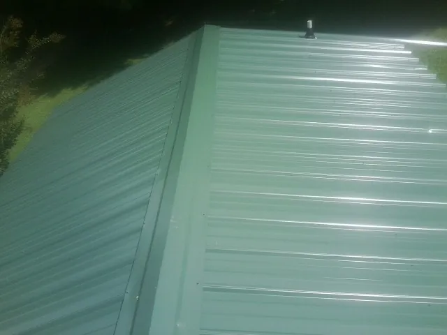 New green metal panels meeting at the ridge of a roof — Flat Roof Repair work by our crew in Rockford