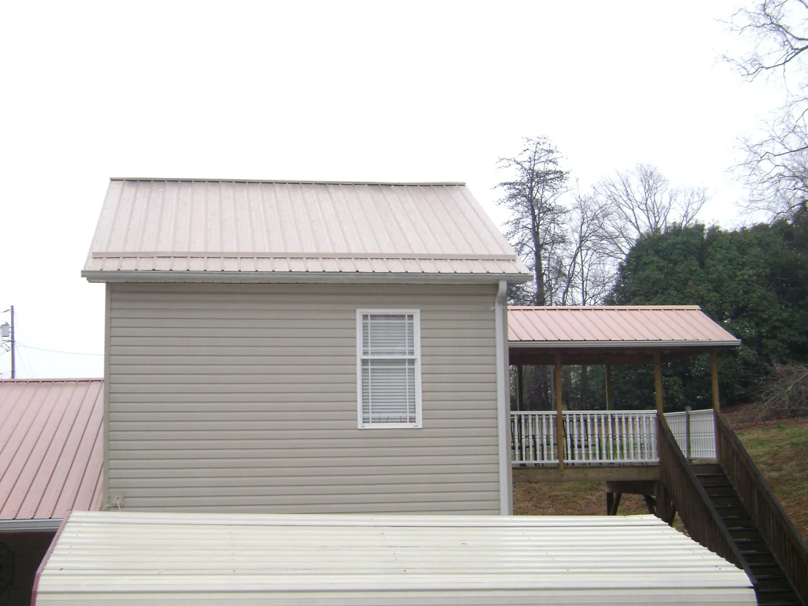 Tan metal roofs on a two story addition and attached porch, from a Roof Replacement job in Rockford